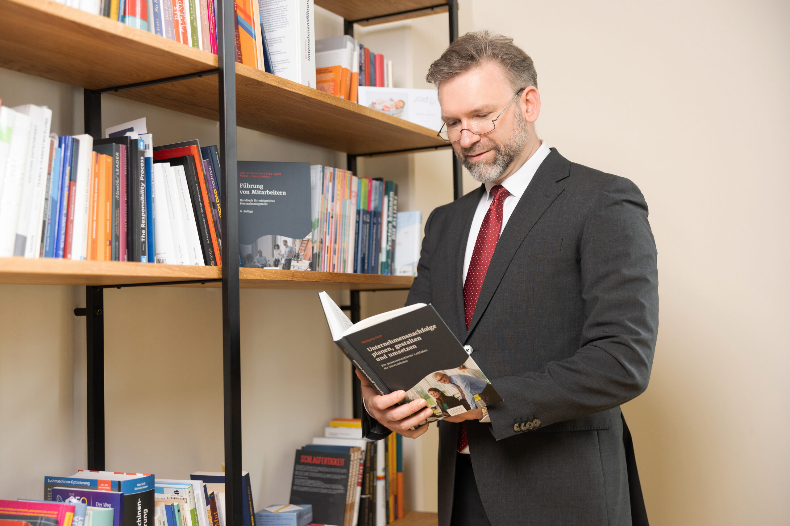 Geschäftsführer Matthias Wolf steht in der Bibliothek des Büros der Goldpfad GmbH in Bautzen und liest ein Buch zum Thema Unternehmensnachfolge